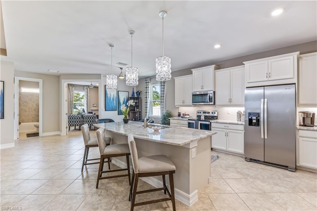 Spacious kitchen featuring an island with stone countertop, white cabinetry with crown molding, stainless steel appliances, and tile flooring