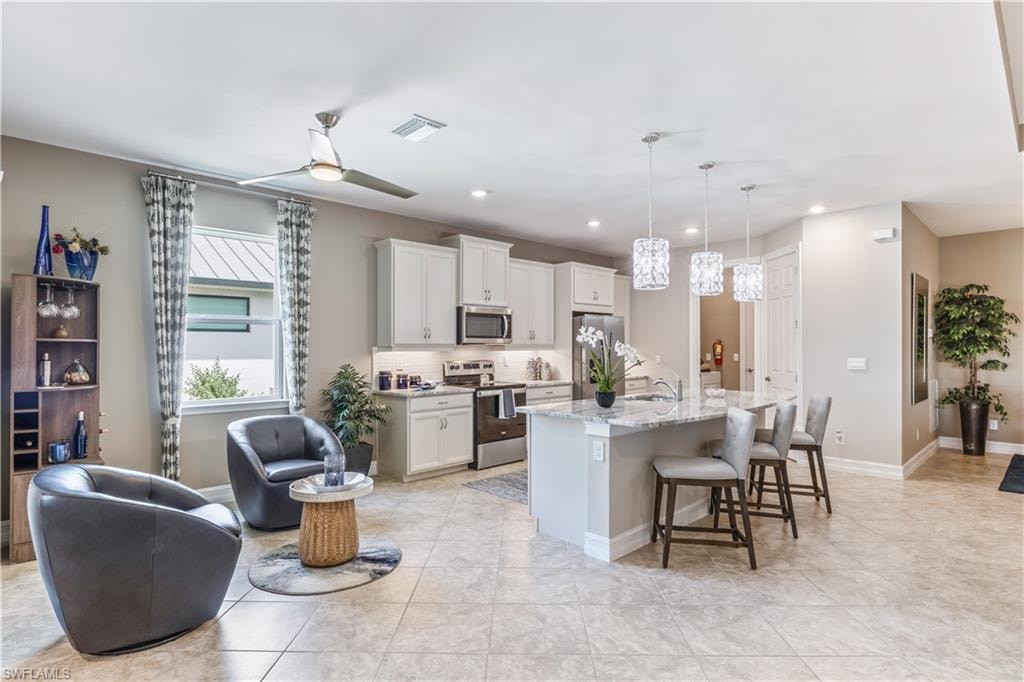 Open-concept living space featuring a chef's kitchen with white cabinetry, stainless steel appliances, and a large waterfall-edge island with seating for multiple guests