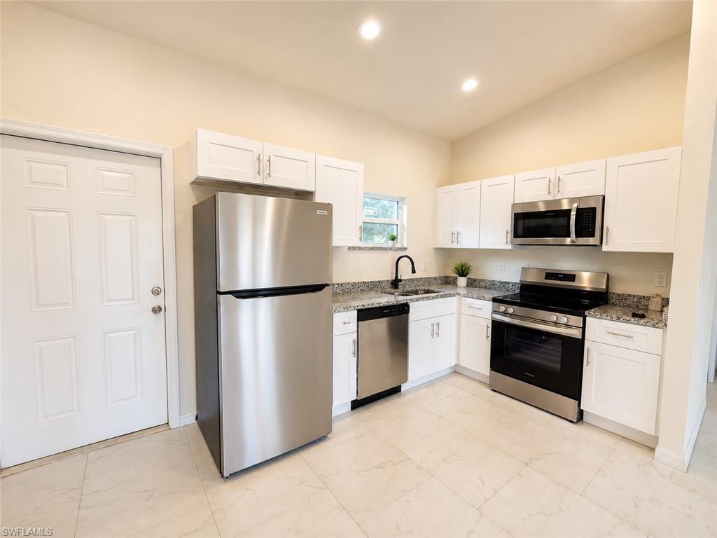 Modern kitchen featuring stainless steel appliances, white cabinetry with chrome hardware, granite countertops, and tile flooring