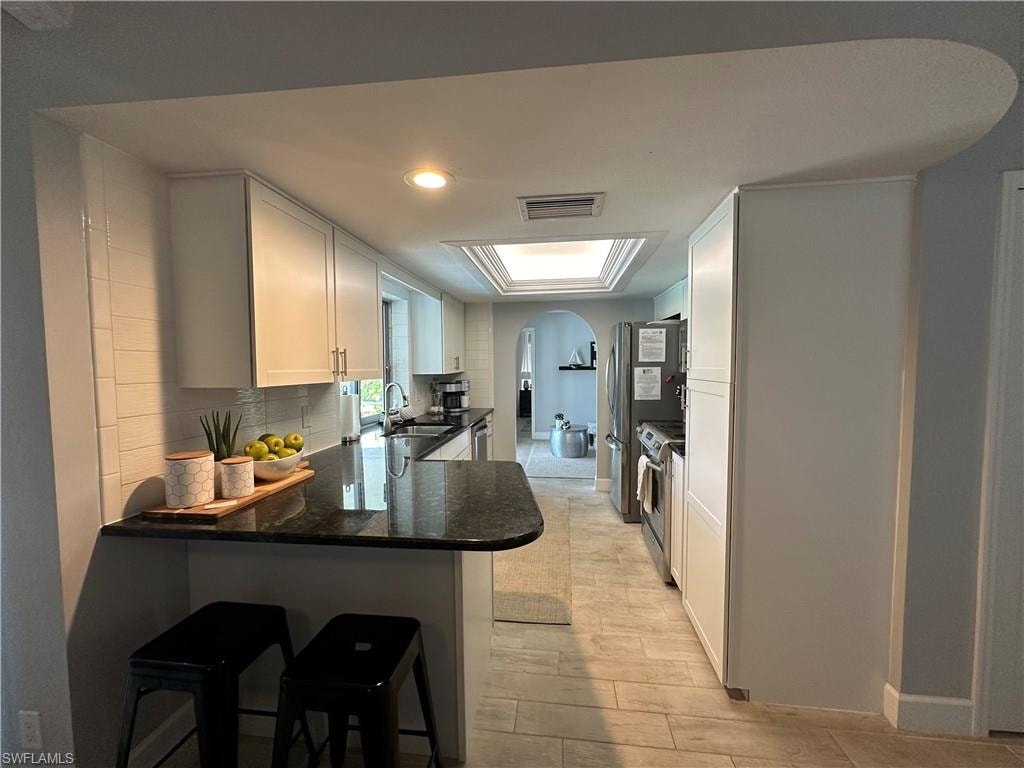 Kitchen featuring decorative backsplash, white cabinetry, a kitchen breakfast bar, and kitchen peninsula