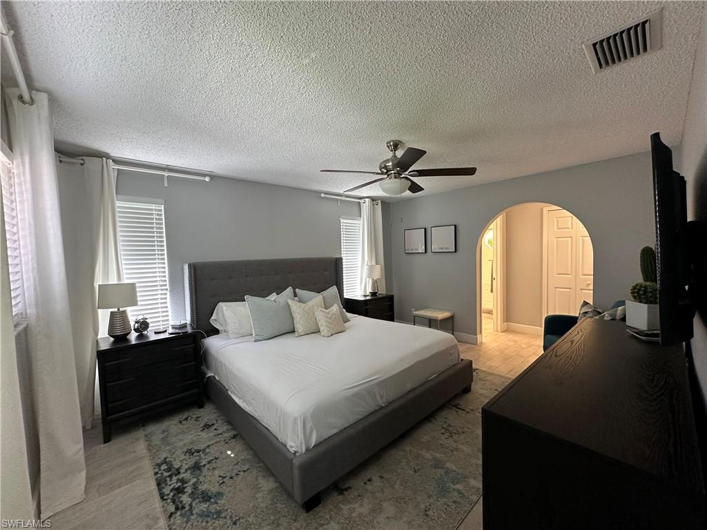 Bedroom featuring ceiling fan, ensuite bath, and a textured ceiling