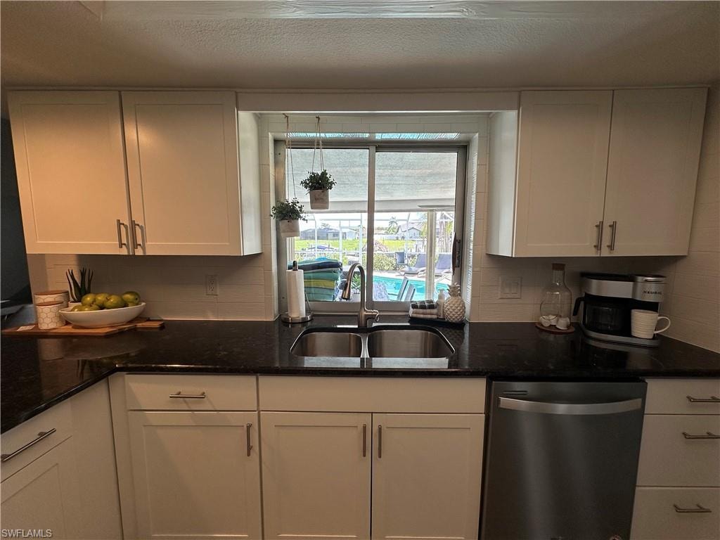 Kitchen featuring sink, stainless steel dishwasher, white cabinetry, and dark stone counters