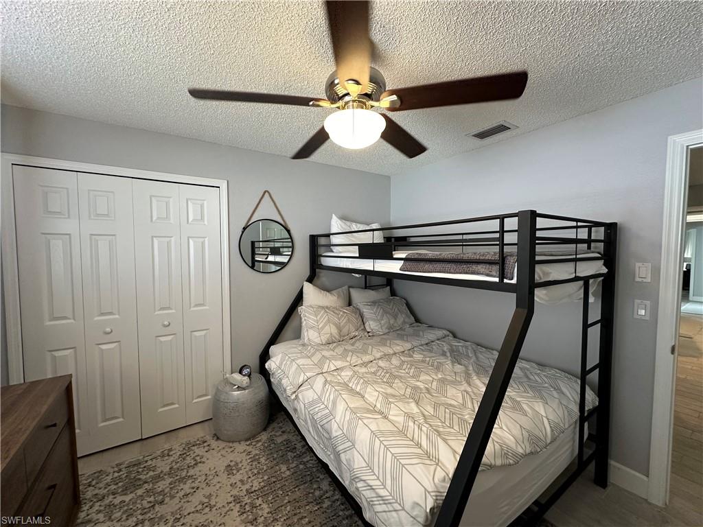 Bedroom with hardwood / wood-style flooring, a textured ceiling, a closet, and ceiling fan