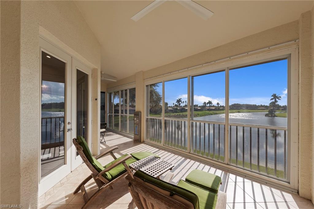 Screened lanai with expansive water views, featuring floor-to-ceiling sliding glass doors, white wood-finish railings, ceiling fan, and direct access to the main residence