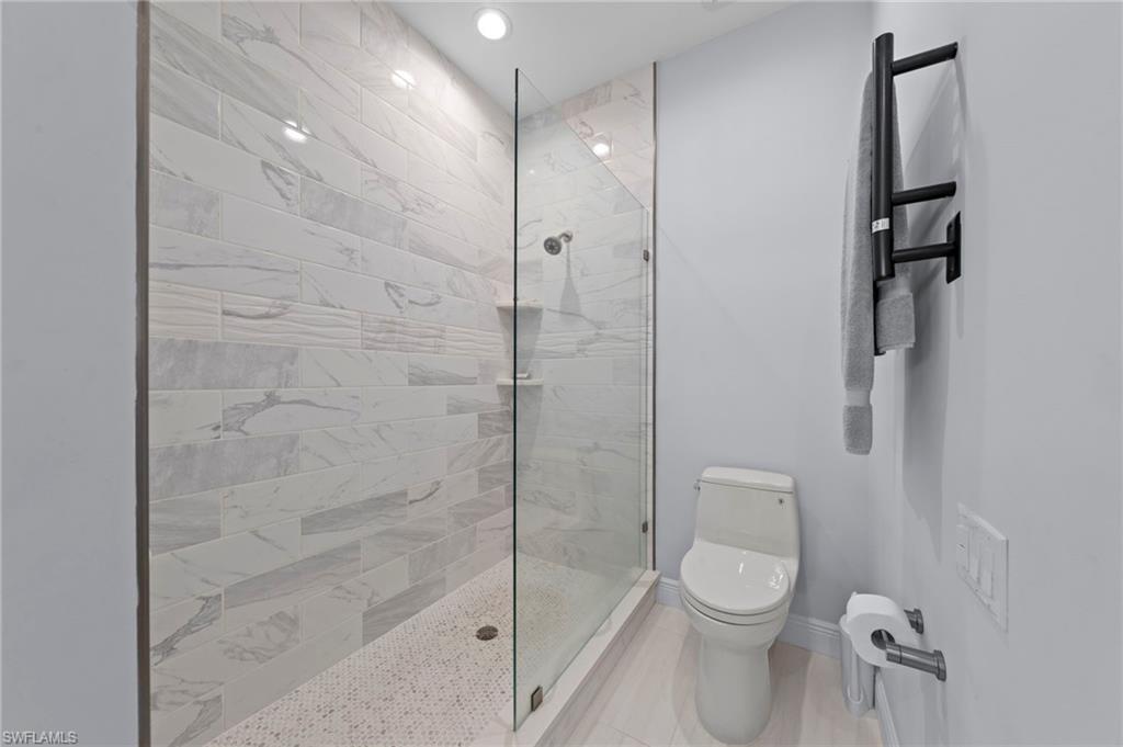 Modern bathroom featuring a frameless glass-enclosed shower with marble-look tile surround, ceramic vessel toilet, and brushed black towel warming rack
