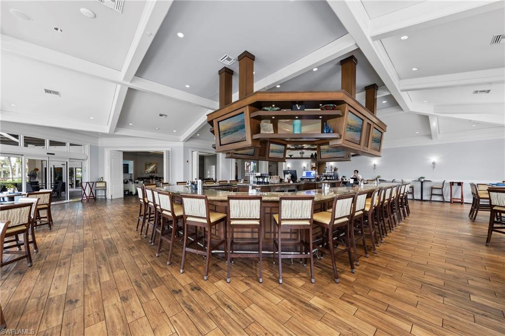 Expansive bar area featuring wood-finish flooring, a large wrap-around bar with seating, a coffered ceiling, recessed lighting, and wall sconces