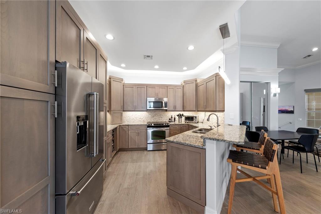 Spacious kitchen featuring warm wood-finish cabinetry, stainless steel appliances including a dual-door refrigerator and gas range, granite countertops, and a large center island with seating