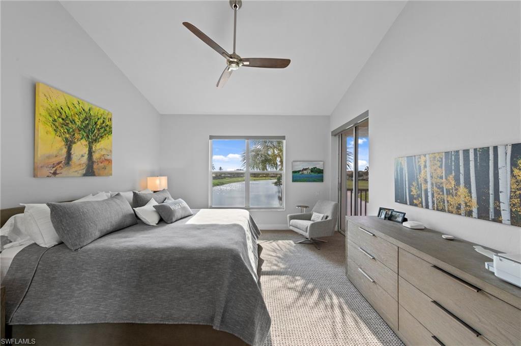 Bright primary bedroom featuring a spacious layout with sliding glass doors opening to outdoor space, light wood-finish dresser with multiple drawers, ceiling fan with brushed metal finish, neutral carpeting, and large windows flooding the room with natural light