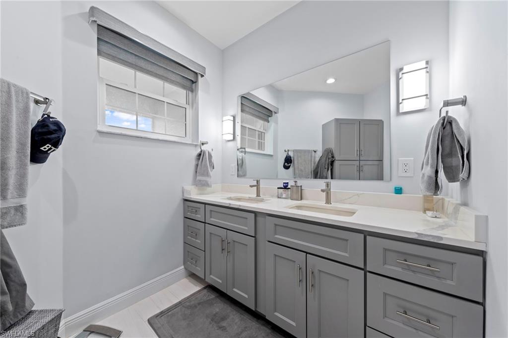 Spa-inspired primary bathroom featuring a dual-sink vanity with gray cabinetry, quartz countertop, and chrome fixtures