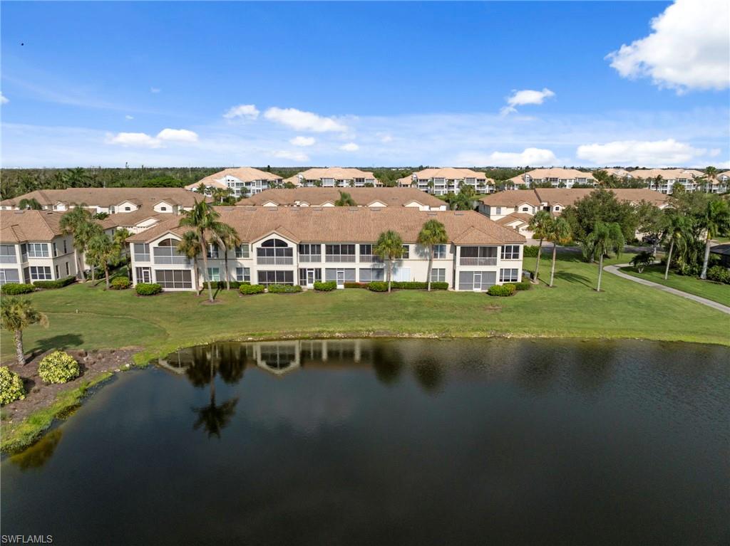 Waterfront condominium building with screened balconies, tile roofing, and a manicured lawn