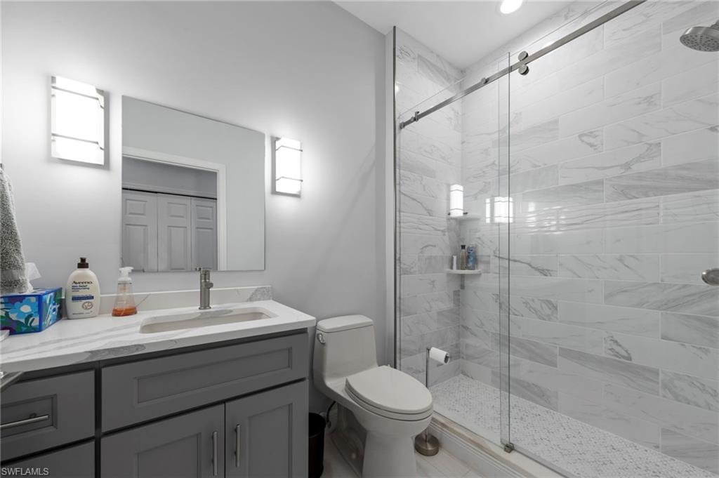 Spa-inspired primary bathroom featuring a frameless glass-enclosed shower with marble-look tile surround, a dark charcoal vanity with white quartz countertop and integrated rectangular sink, chrome fixtures, recessed lighting, and a separate toilet compartment