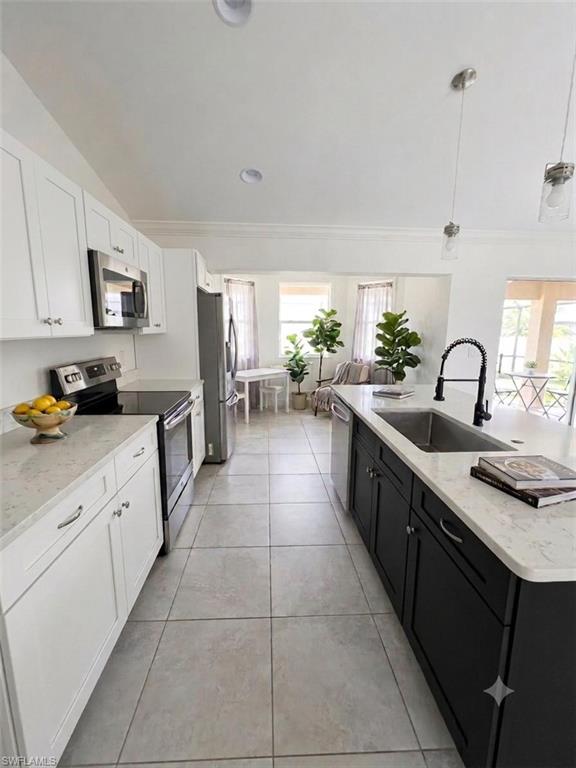Galley kitchen featuring white cabinetry with hardware accents, stainless steel appliances including a built-in microwave, quartz countertops, a large island with contrasting black cabinetry and undermount sink with pull-down faucet, and tile flooring throughout