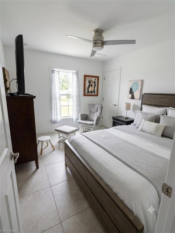 Bedroom featuring light-toned tile flooring, a window with sheer curtains, a modern ceiling fan with integrated lighting, and a white paneled door