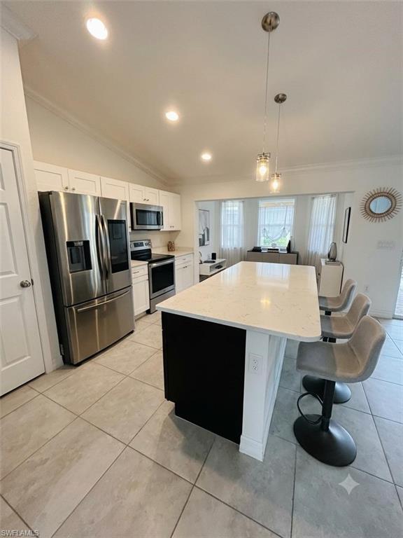 Modern kitchen featuring a large central island with seating, stainless steel appliances, white cabinetry, vaulted ceilings, and recessed lighting