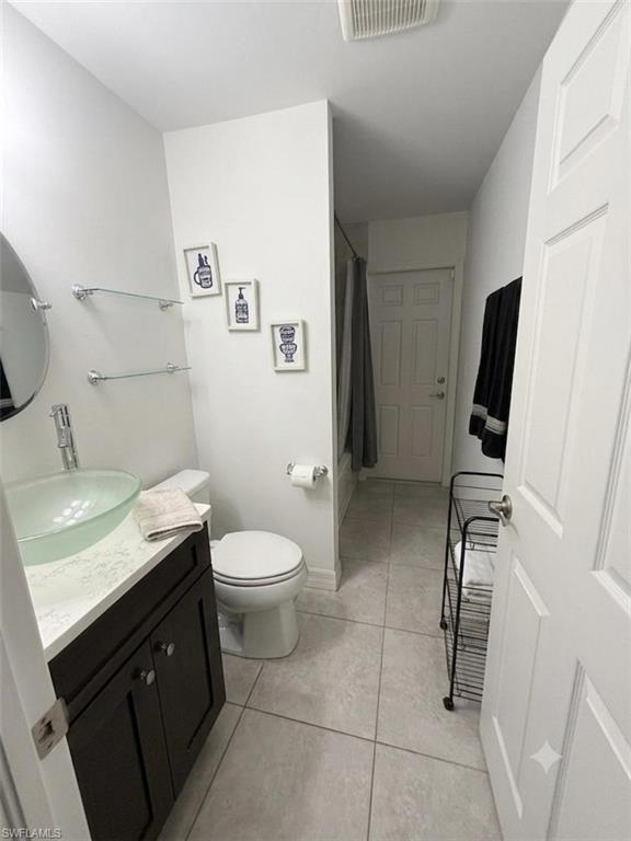 Efficient full bathroom featuring a dark vanity with integrated sink, ceramic tile flooring, toilet, and framed mirror