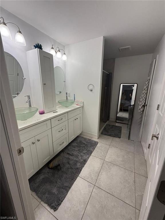 Spacious primary bathroom featuring dual vanity with ample storage cabinetry, ceramic tile flooring, sconce lighting, and generous countertop space