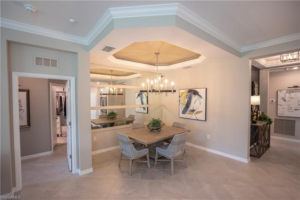 Dining area featuring a tray ceiling with crown molding, a multi-light chandelier, and a mirrored accent wall