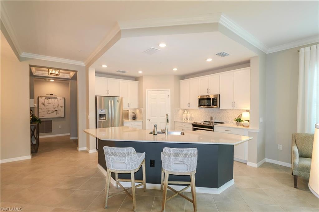 Kitchen featuring a multi-sided island with a built-in sink, stainless steel appliances, white cabinetry, and tile flooring