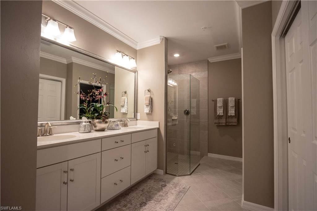 Dual sink vanity with white cabinetry and chrome hardware, featuring a large mirror and overhead lighting