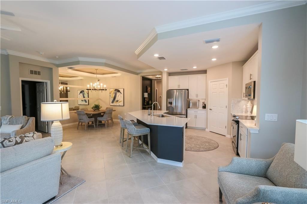 Open-concept living space with light-toned tile flooring, recessed lighting, white cabinetry, a kitchen island with seating, and a formal dining area featuring a chandelier