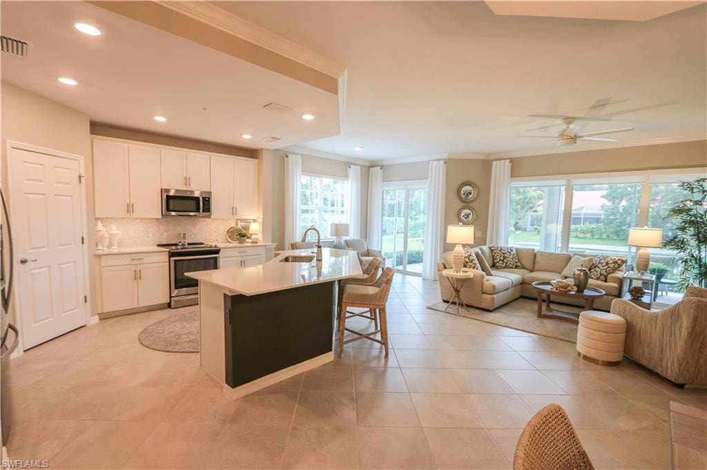 Open-concept layout featuring a kitchen with white cabinetry, stainless steel appliances, and an island with seating