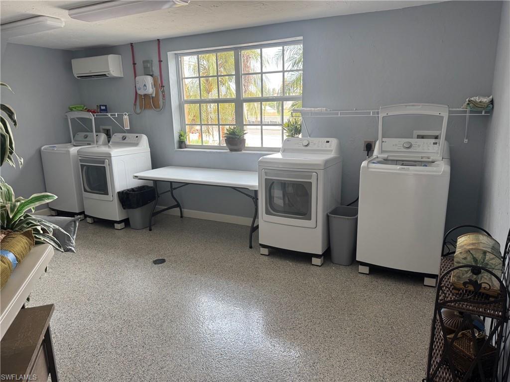 Spacious utility room featuring multiple laundry machines, a window for natural light, wall-mounted shelving, durable speckled flooring, and light blue-gray painted walls