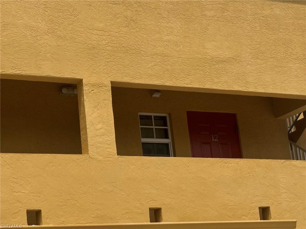 Exterior stucco facade featuring a red entrance door with visible numbering and a white-framed window
