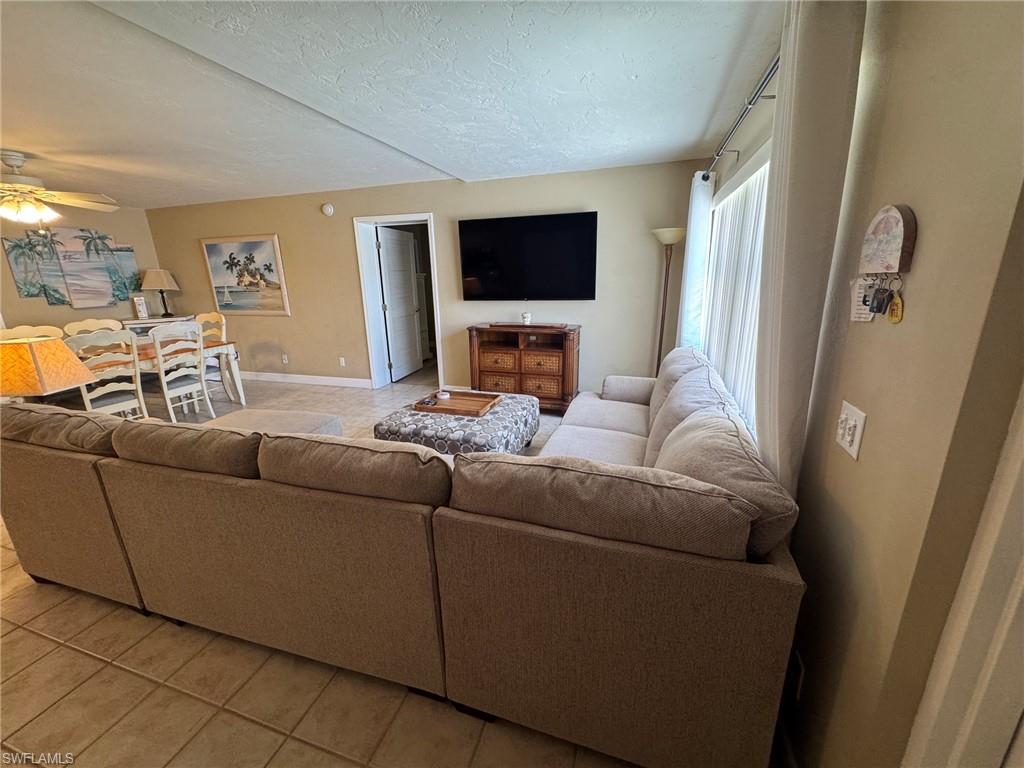 Open-concept living space featuring ceramic tile flooring, a dining area with a ceiling fan, and a wall-mounted television over a wood-finish media console