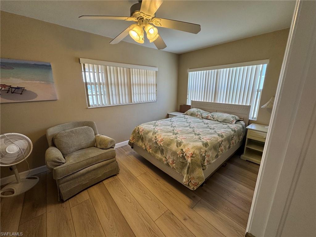 Bedroom featuring wood-finish tile flooring, two large windows with vertical blinds, a ceiling fan with integrated lighting, and neutral wall tones