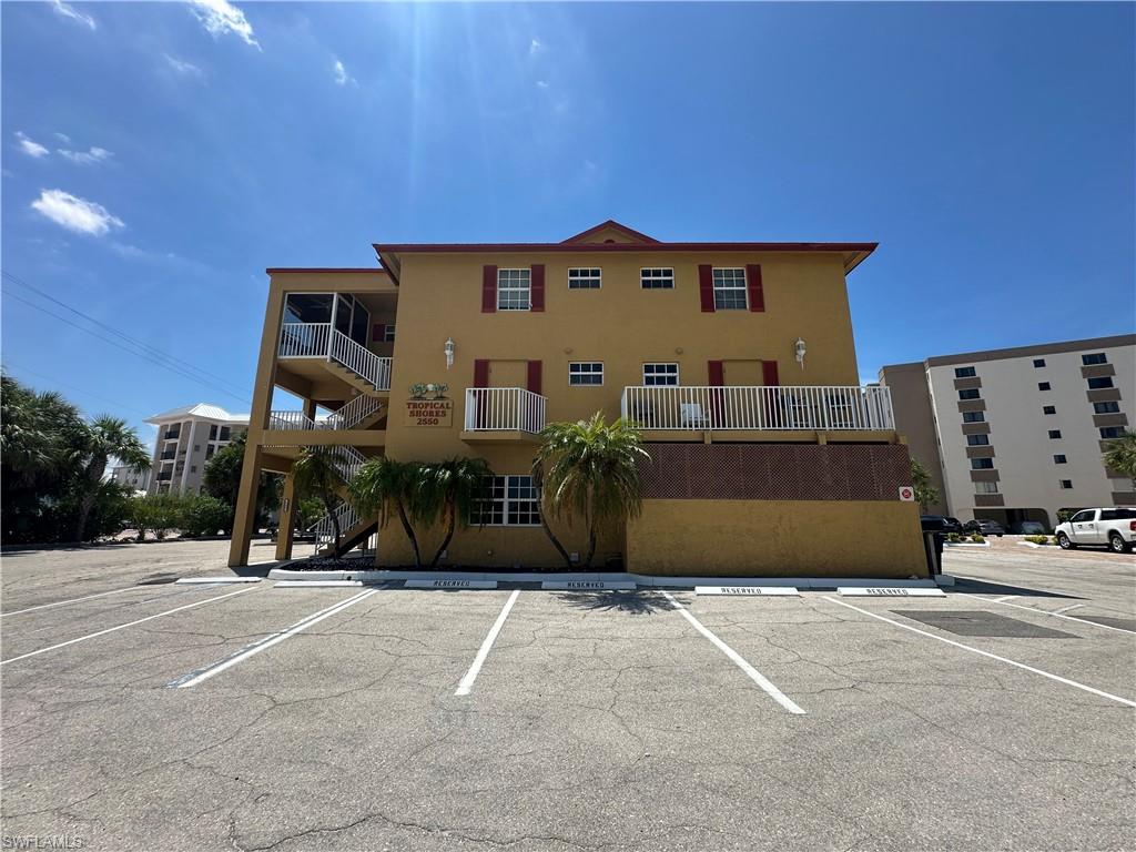Two-story building with a stucco exterior, exterior staircases, multiple balconies, and a paved parking area