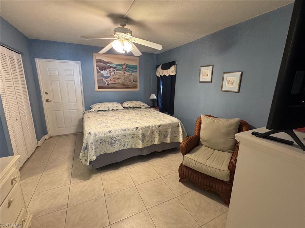 Bedroom featuring a ceiling fan with integrated lighting, tile flooring, and a louvered bi-fold closet door