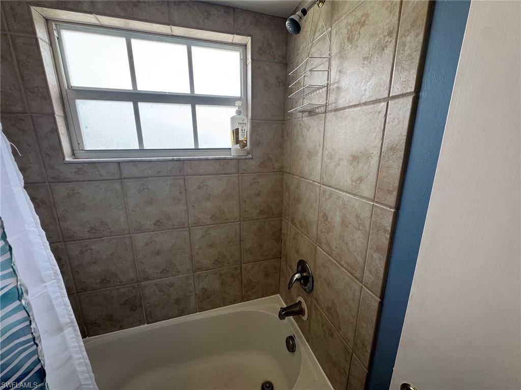 Tub and shower combination featuring a tiled surround, frosted window, and chrome fixtures