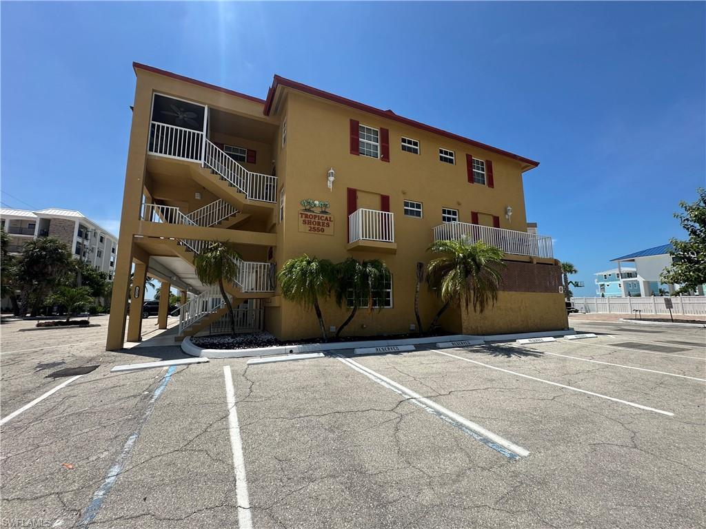 Multi-story building featuring exterior walkways and balconies, red window shutters, and designated parking spaces