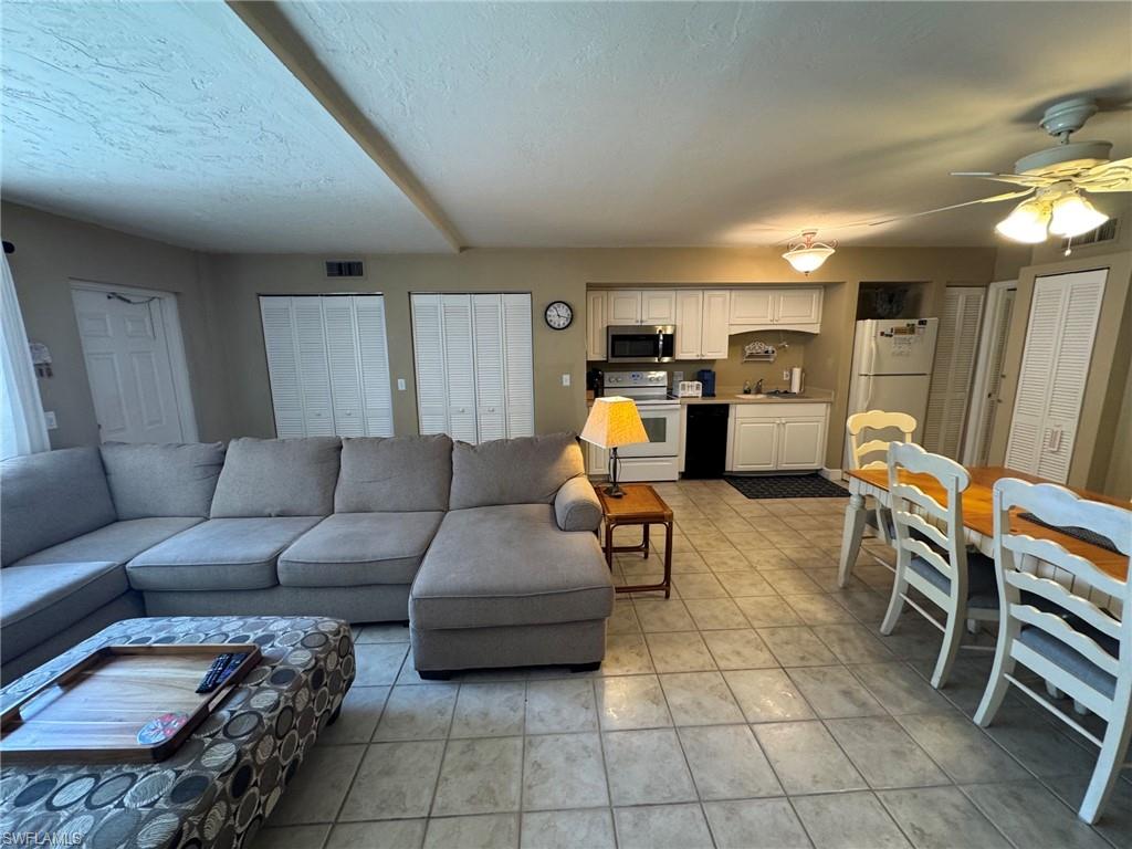 Open-concept living space featuring ceramic tile flooring, kitchen with white cabinetry and stainless steel & white appliances, dining area, and multiple built-in storage closets