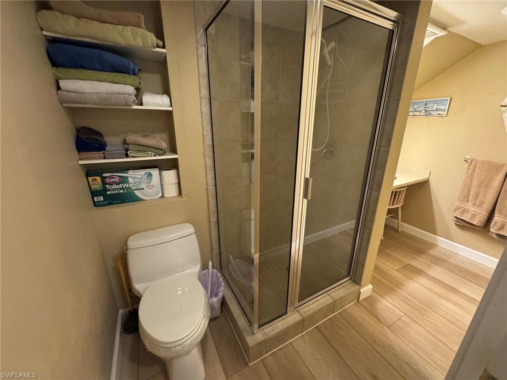 Bathroom featuring a glass-enclosed shower, wood-finish flooring, built-in shelving, and a white toilet