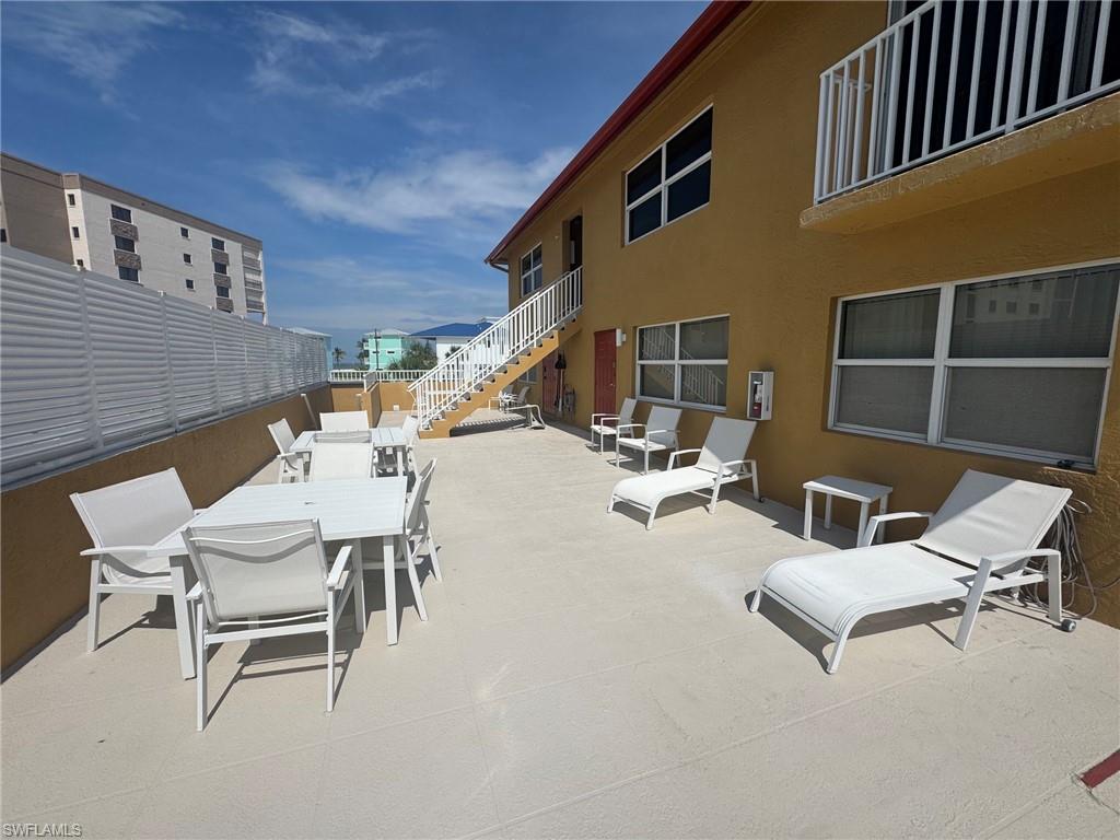 Exterior terrace featuring ample concrete paving, a white slatted privacy fence, and an external staircase