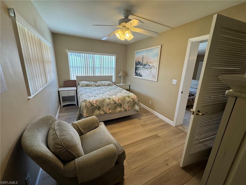 Bedroom featuring wood-finish tile flooring, a ceiling fan with integrated lighting, and multiple windows with vertical blinds