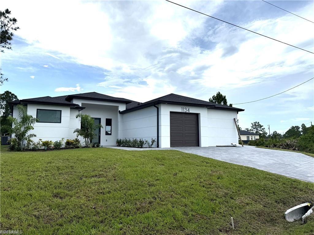 Contemporary white exterior featuring a dark brown garage door, dark roof, and a patterned paver driveway