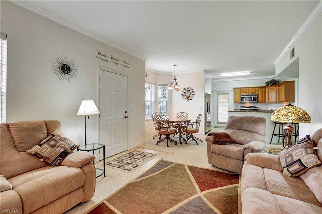 Open-concept living area featuring multiple seating zones with upholstered recliners, hardwood-finish flooring, geometric area rugs, and pendant lighting