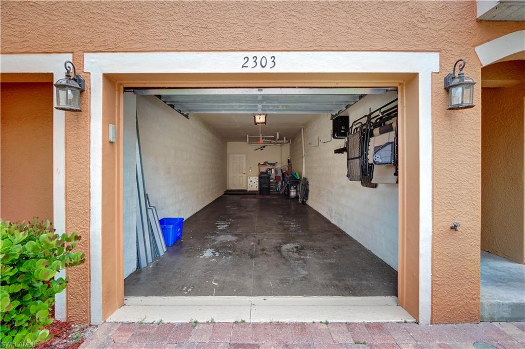 Attached tandem garage featuring ample storage space, concrete flooring, wall-mounted organizational systems, and dual carriage-style garage doors with integrated lighting fixtures