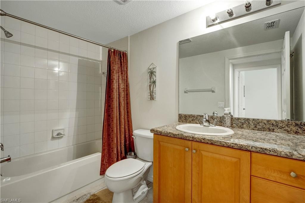Spa-inspired bathroom featuring a wood-finish vanity with dual-sink granite countertop, large framed mirror with integrated lighting, and a separate soaking tub with red fabric shower curtain