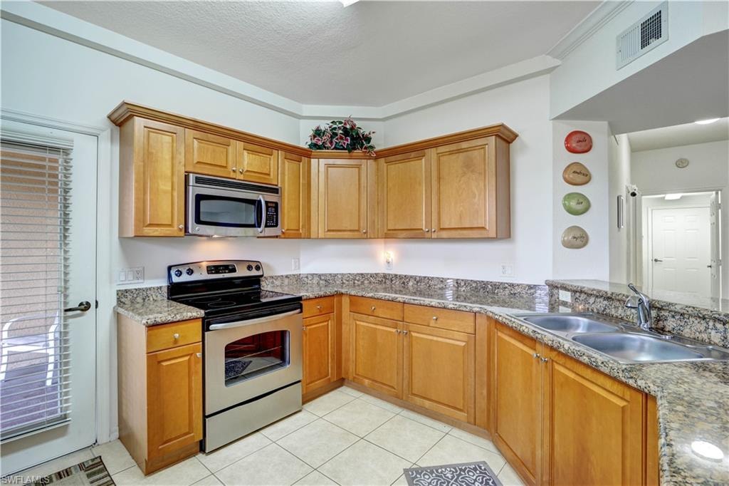 Kitchen featuring light wood cabinetry, granite countertops, stainless steel appliances, a double basin sink, and tile flooring