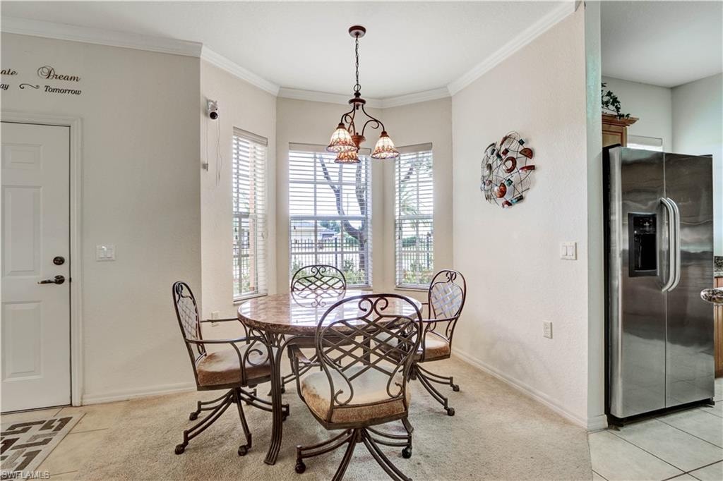 Bright dining area showcasing a curved bay window with plantation shutters, pendant lighting fixture, and direct access to the kitchen featuring stainless steel appliances