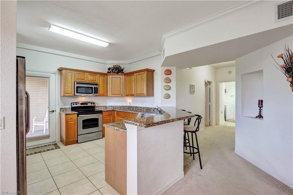 Open-concept kitchen and living area featuring wood-finish cabinetry, stainless steel appliances, granite-style countertops, and a center island with seating