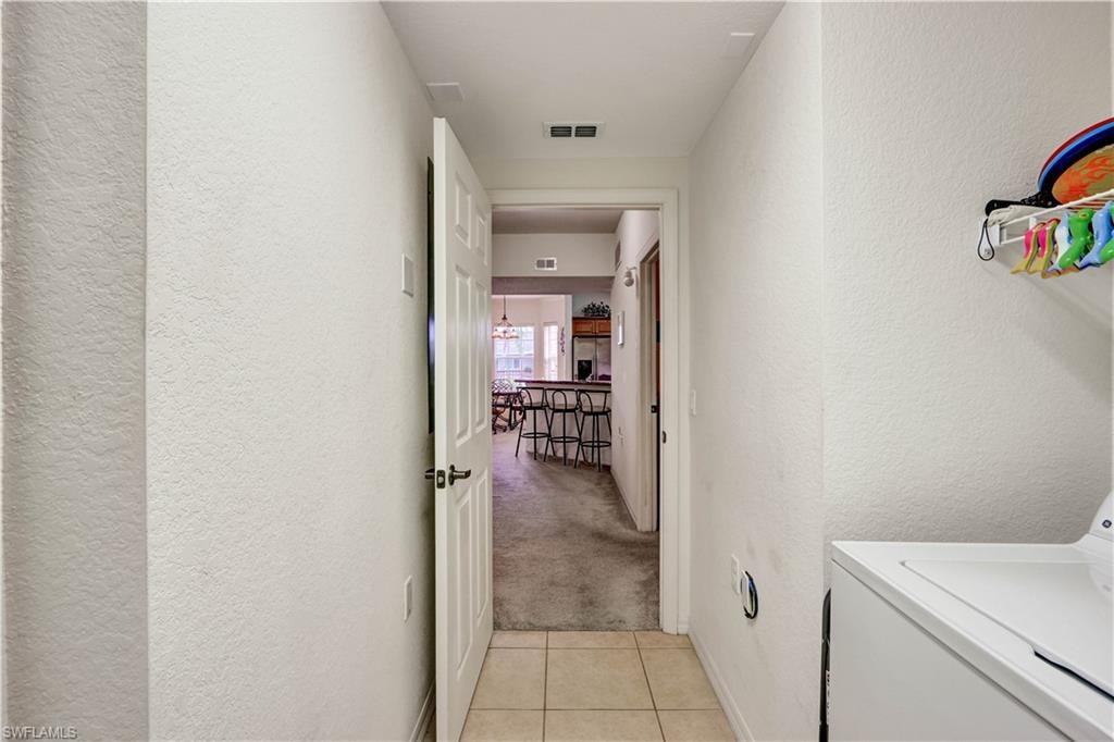 Convenient laundry room featuring tile flooring, white cabinetry, and direct access to the kitchen and living areas