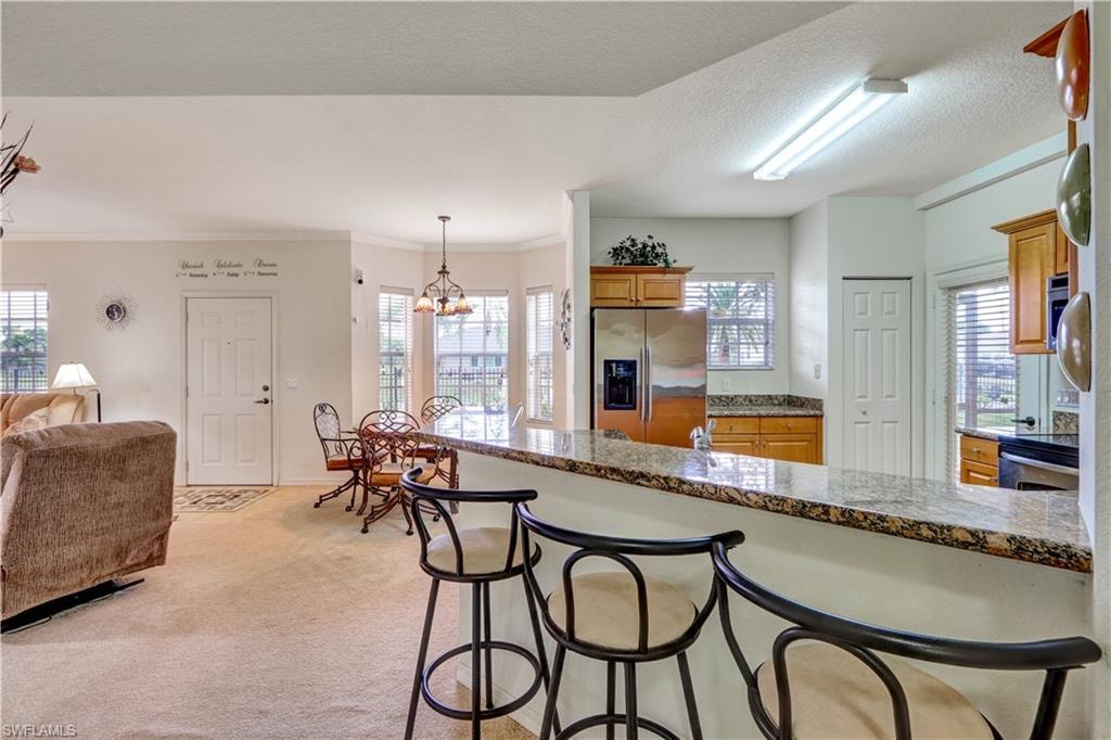 Kitchen bar with granite countertop and seating for three, featuring stainless steel appliances, wood cabinetry, and a dining area with a multi-light chandelier