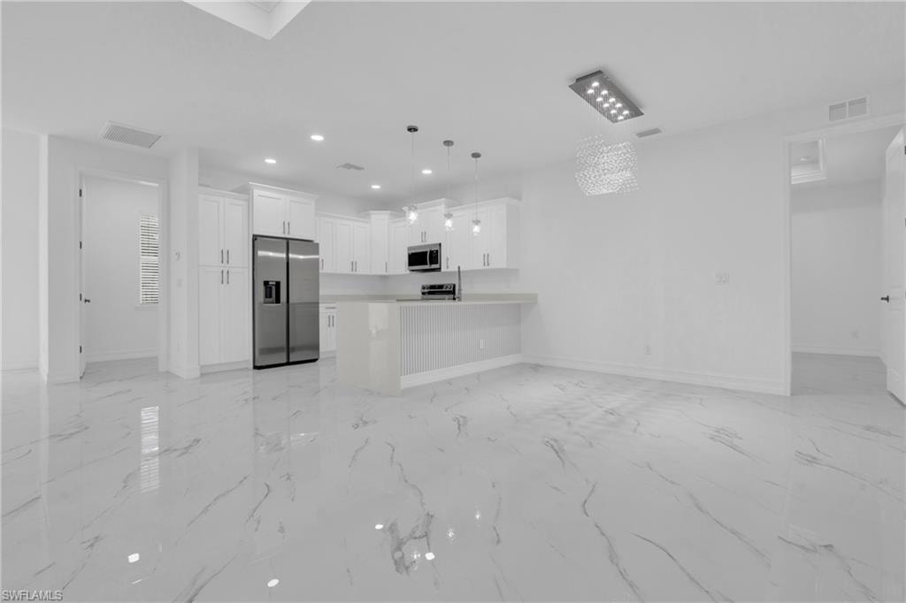 Kitchen with open floor plan, white cabinets, light countertops, stainless steel appliances, and pendant lighting