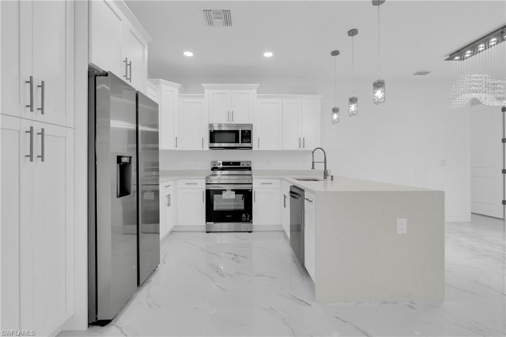 Kitchen with a peninsula, appliances with stainless steel finishes, white cabinets, light stone counters, and recessed lighting