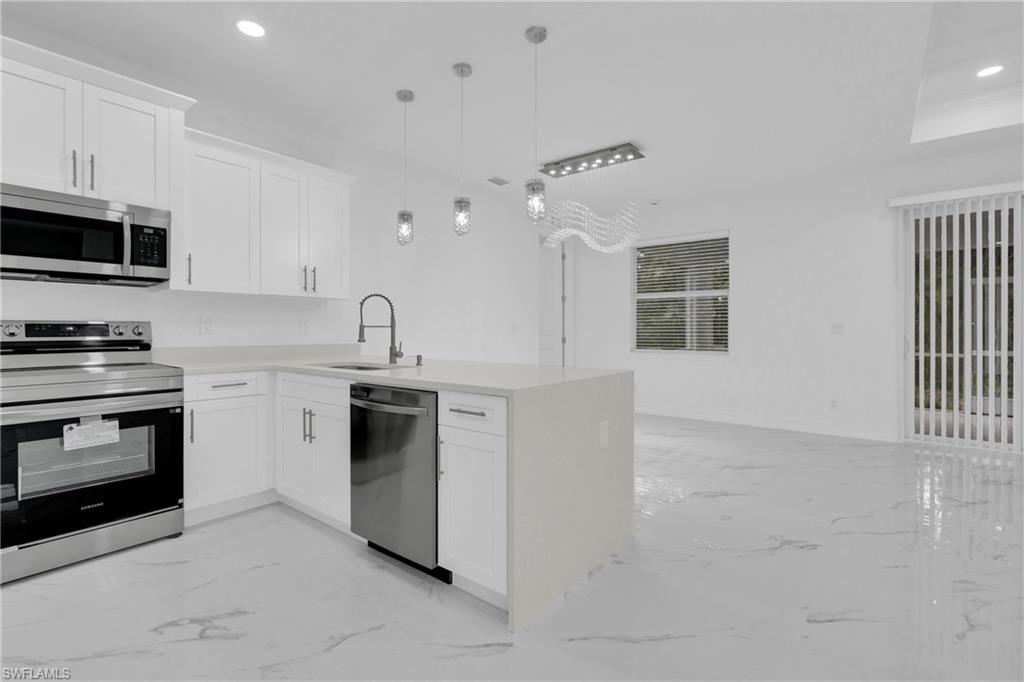 Kitchen featuring appliances with stainless steel finishes, white cabinets, a peninsula, recessed lighting, and light marble finish floors