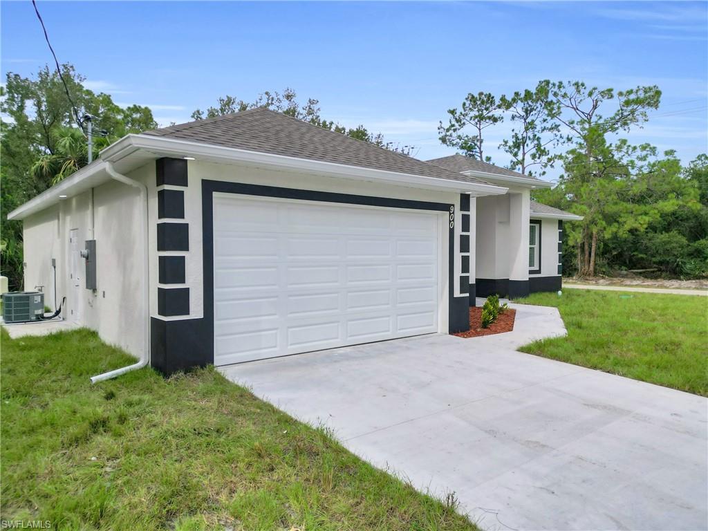 View of front of property featuring a front lawn, concrete driveway, stucco siding, and roof with shingles
